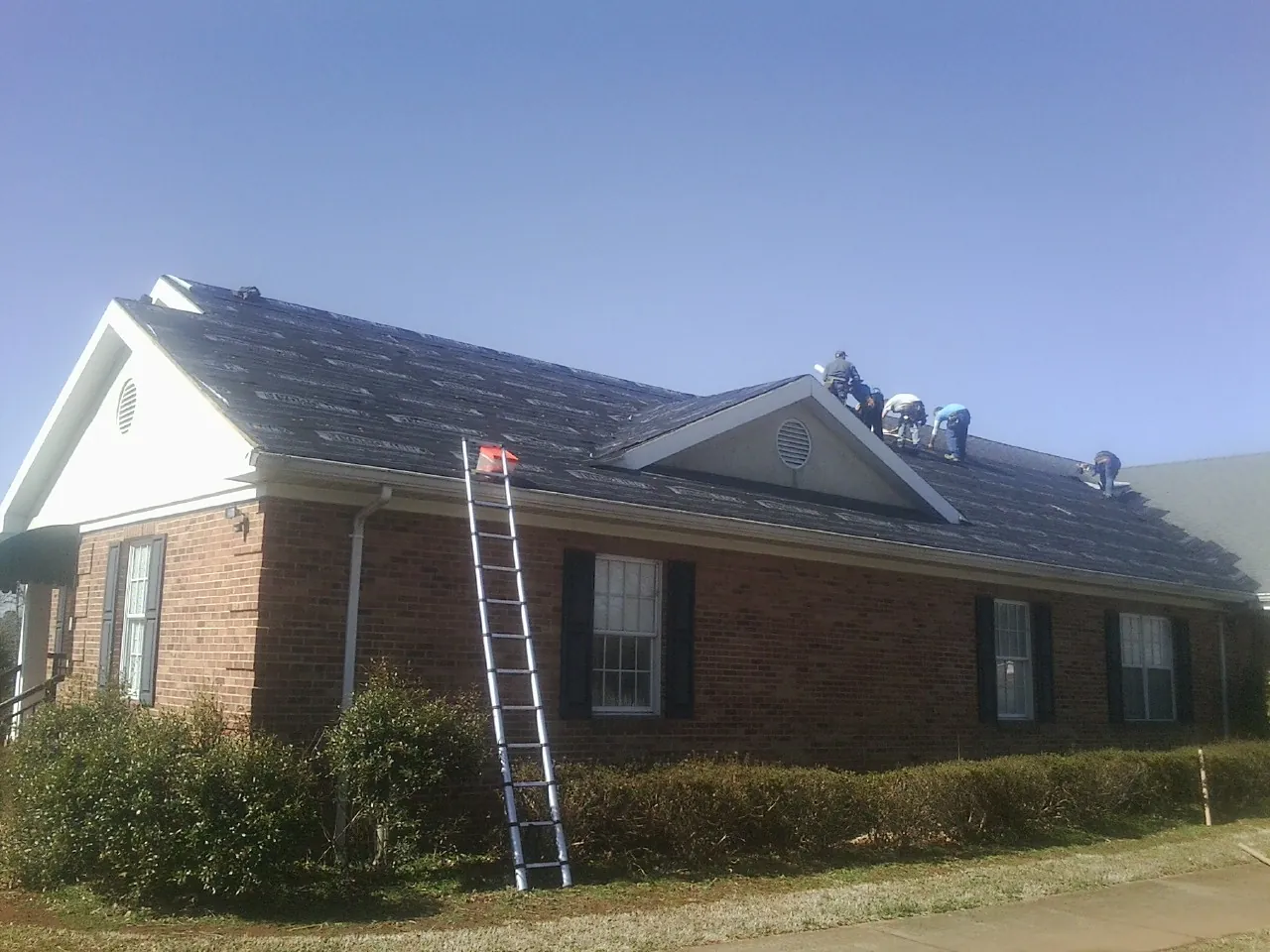 Crew tearing shingles off a brick ranch roof with a ladder set — Metal Roof Repair work by our crew in Mc Donald