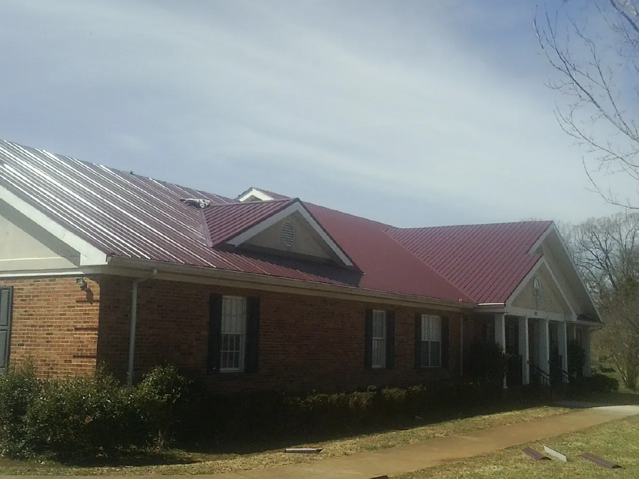 Red metal roof with gabled entries on a long brick building, from a Hail Damage Roof Repair job in Mc Donald