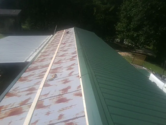 Old rusted panels beside newly installed green metal roofing — Wind Damage Roof Repair by Roofing Brothers in Mc Donald