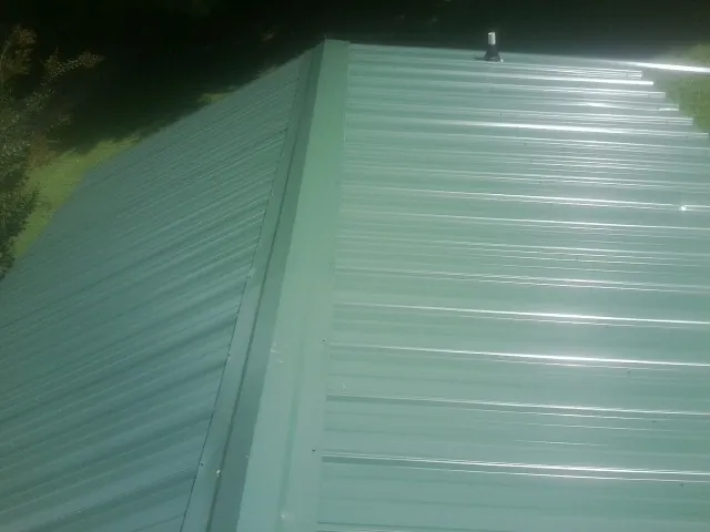 New green metal panels meeting at the ridge of a roof — Flat Roof Repair work by our crew in Mc Donald