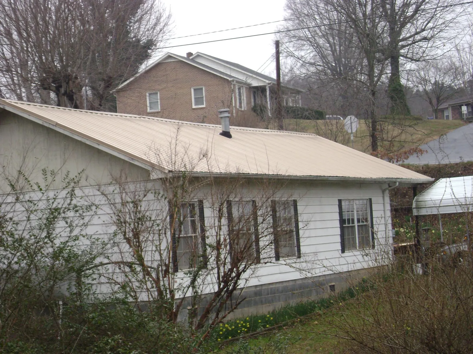 Tan metal roof on a white sided house set into a hillside — Commercial Roofing by Roofing Brothers in Mc Donald